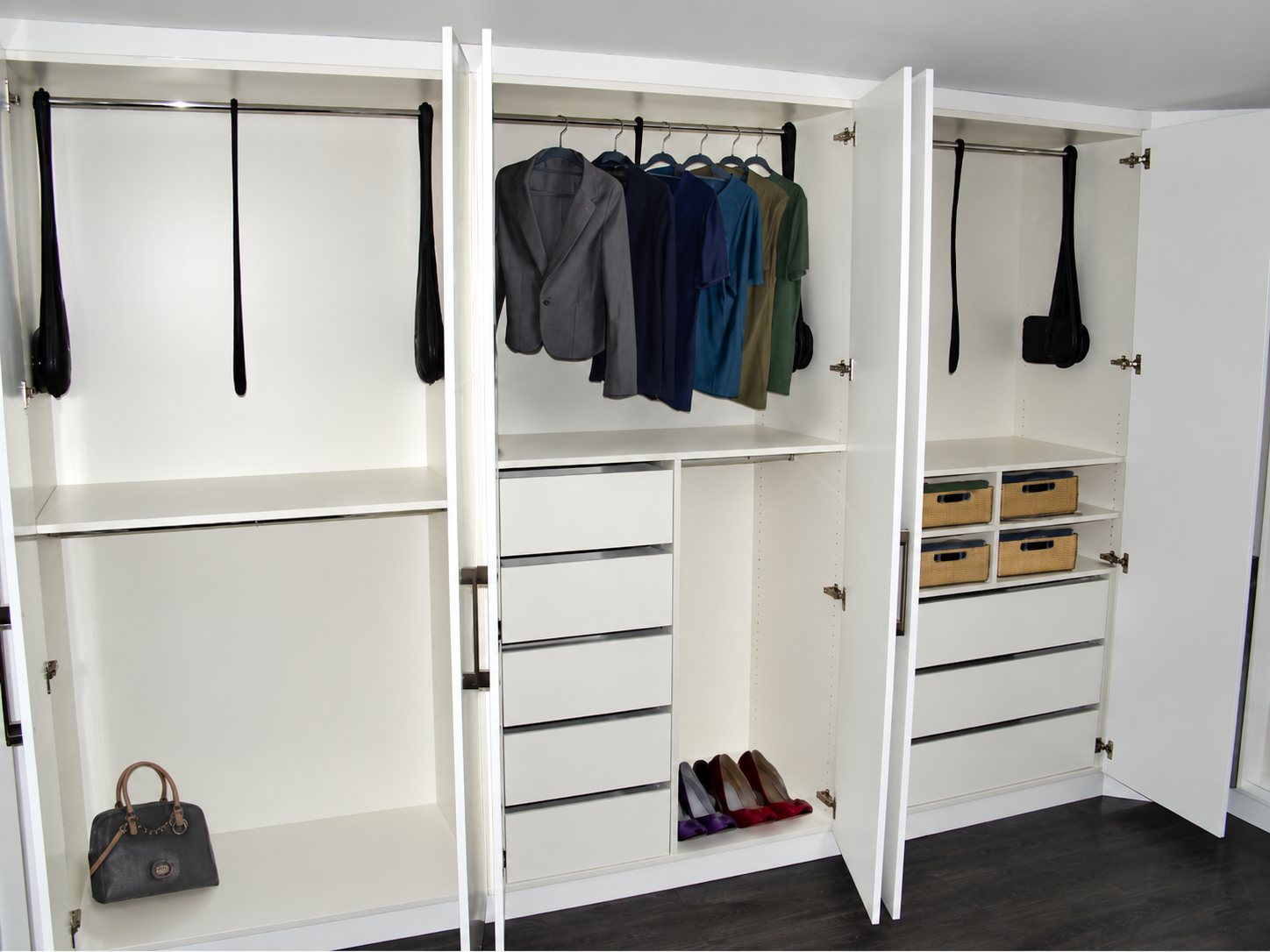 Un grand placard dressing blanc aux portes ouvertes, avec penderies, tiroirs, étagères, vêtements suspendus, un sac à main et des chaussures.