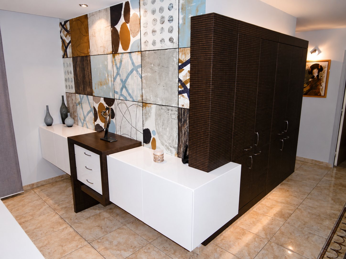 Un agencement sur mesure composé d'un buffet suspendu blanc laqué, d'un petit meuble à tiroirs et d'une grande armoire en bois foncé devant un mur de carreaux décoratifs.