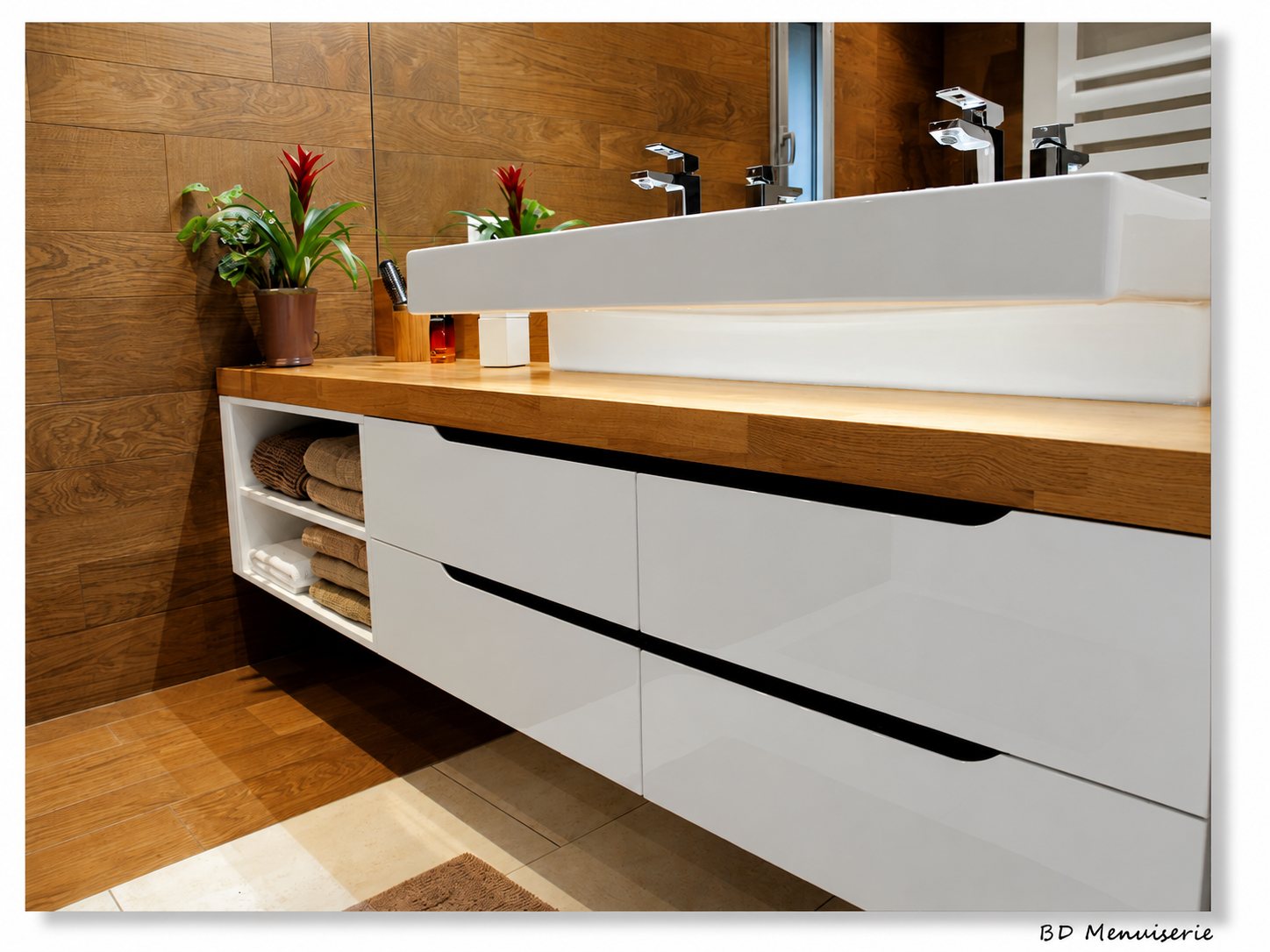 Meuble vasque suspendu laqué blanc avec tiroirs sans poignée, plan de travail en bois et niche de rangement pour serviettes dans une salle de bain aux murs effet bois.